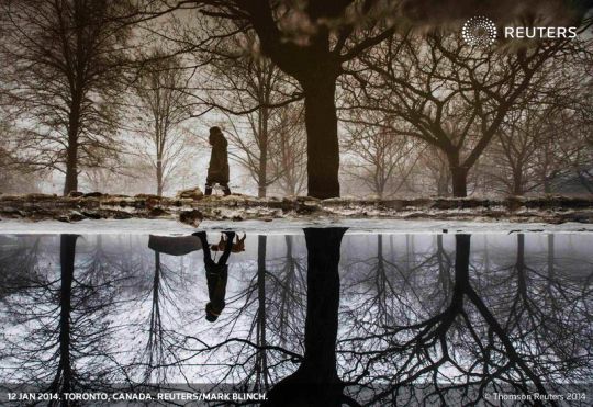 A woman is reflected in a puddle from rain and melted ice as she walks her dog in Toronto